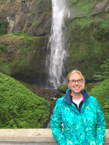The blonde version of Dr. Feldner smiles in front of a beautiful waterfall.
