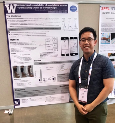 Brandon Nguyen standing in front of his poster at RehabWeek wearing a dark blue shirt. His poster features images of the smartphone app and graphs.