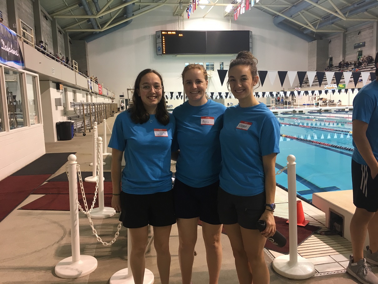 3 students stand in front of a pool in blue shirt at Special Olympics.