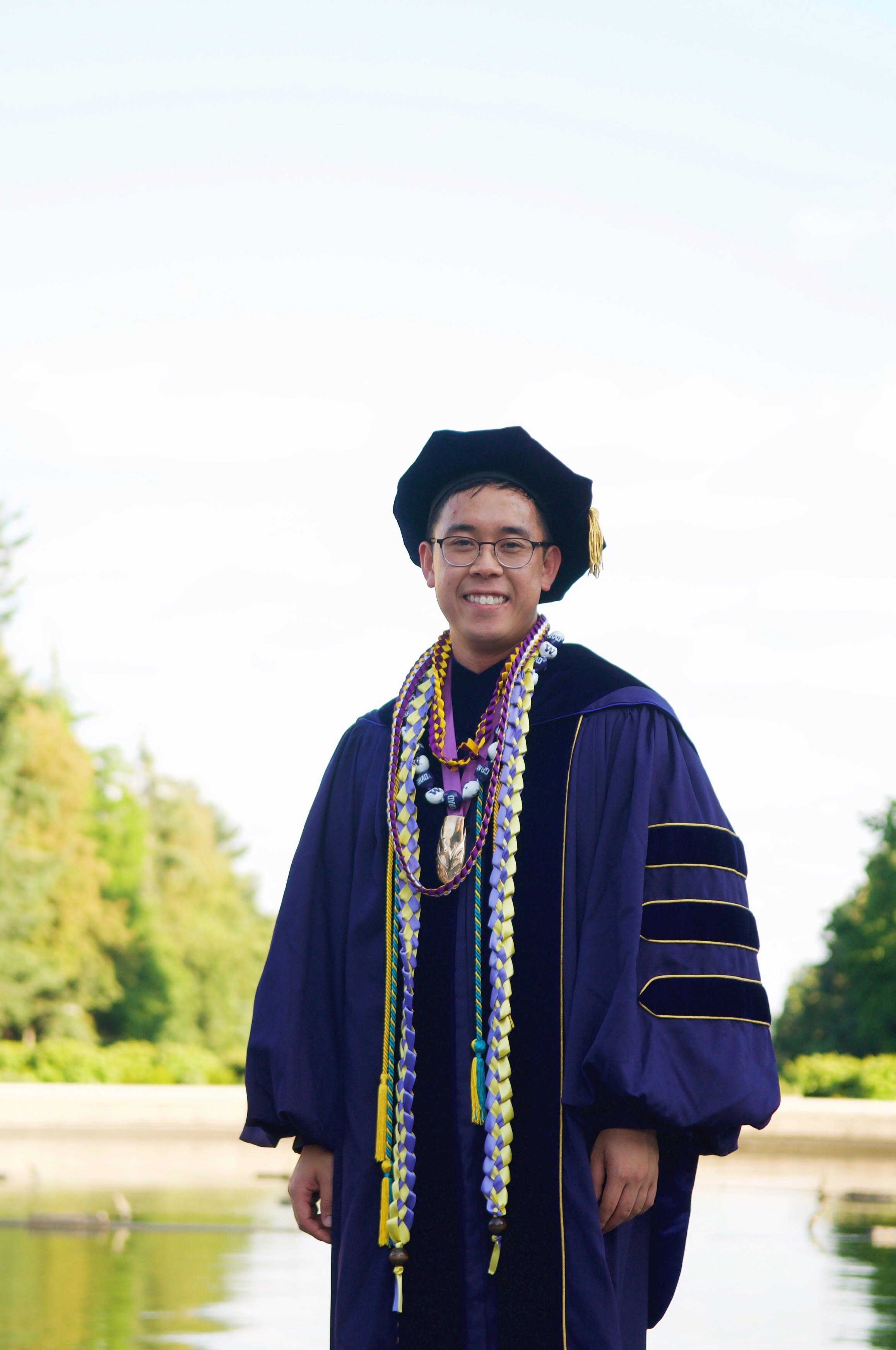 Brandon dressed in his purple graduation regalia in front of the UW fountain