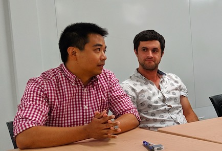 One of the patent examiners in a red checkered shirt answers students questions. He is seated at a table with hands clasped in front of him.