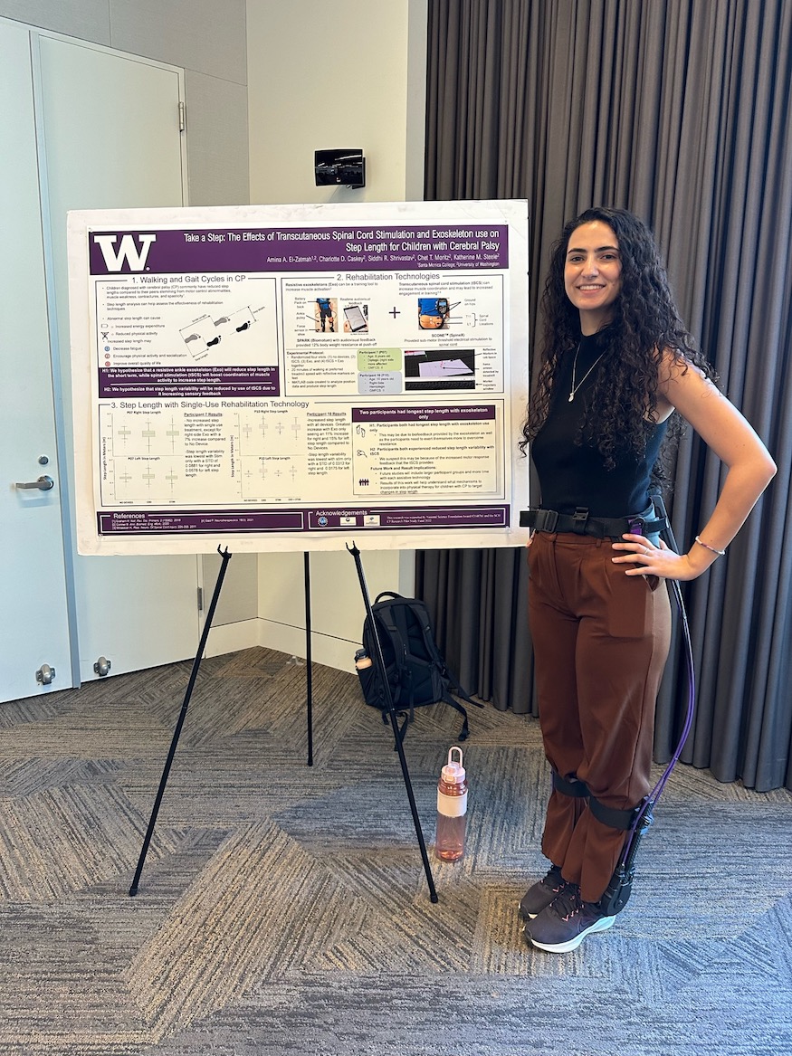 Amina is wearing the Biomotum Spark exoskeleton while standing in front of her poster at her CNT presentation.