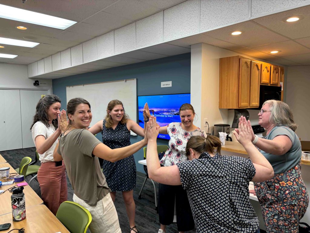 A diverse group of individuals enthusiastically raising their hands to high five and connect their hands to activate a DIY switch.