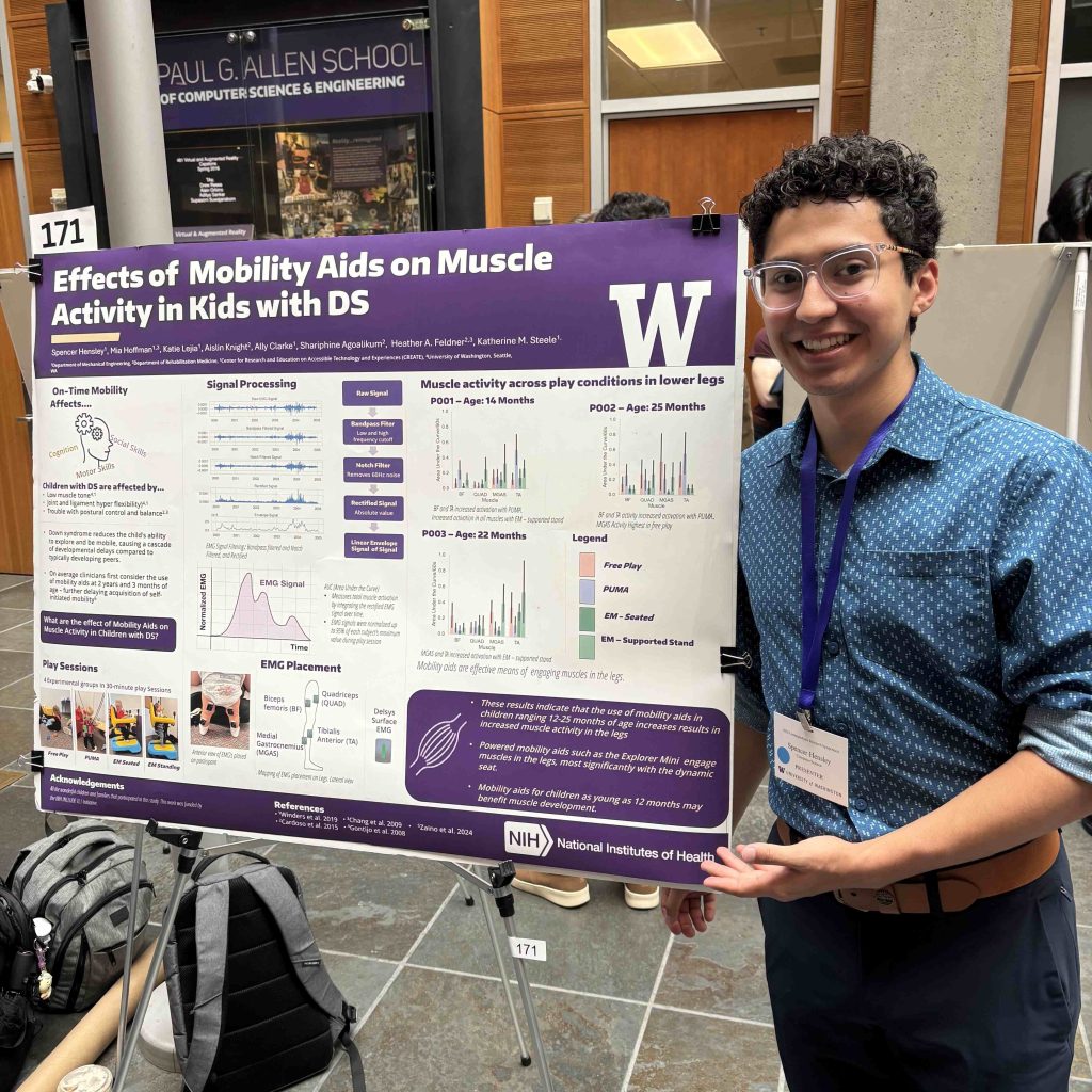 A person stands beside a scientific poster titled “Effects of Mobility Aids on Muscle Activity in Kids with DS.”