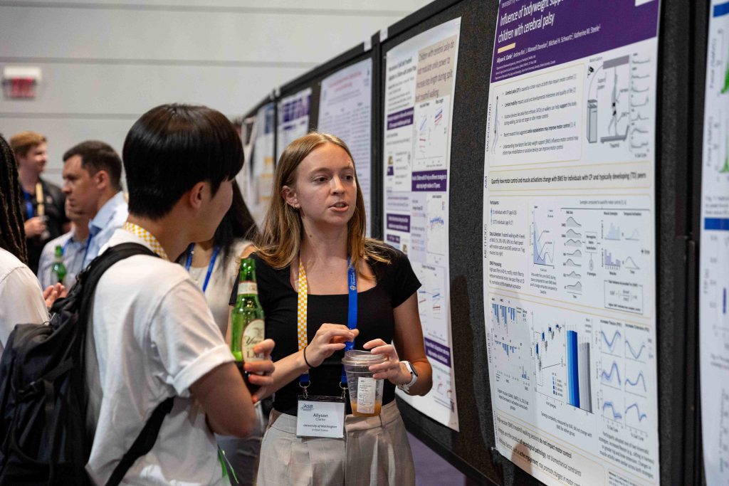 Researcher presenting findings to an attendee in front of scientific posters at ASB 2025, showcasing graphs and charts related to biomechanics research.