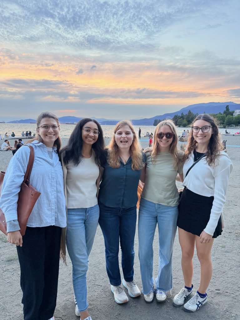 Ally, Mackenzie, Mia, Ally, and Maddie stand on a beach at sunset.